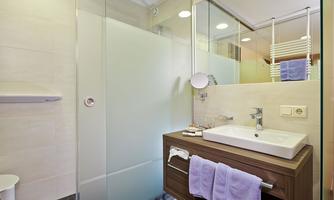 A modern bathroom with a clear shower cabin and an elegant sink. There are also towels in purple and a bright, friendly atmosphere.