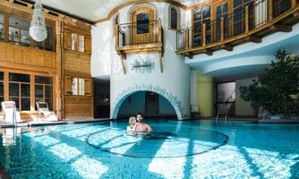 A luxurious indoor pool with clear water and modern wooden elements. Surrounded by windows and plants, the space creates a relaxing atmosphere.