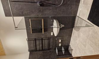 A modern bathroom with a glass shower partition. The walls are in dark colors, and there is a stylish sink arrangement.