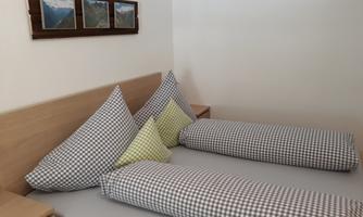 A cozy bedroom with a wooden bed and checked pillows. Pictures of mountains hang on the wall.
