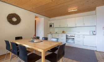 A modern kitchen with a large dining table and black chairs. The walls are light and the floor is made of wood, creating an inviting atmosphere.