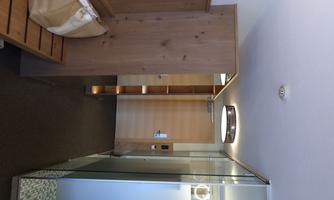 A modern hotel room with a bright entrance area. There are wooden shelves and a glass wall that separates a bathroom area.