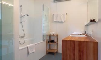 A modern bathroom with a clear shower partition and a wooden sink unit. There are towels and a minimalist style.