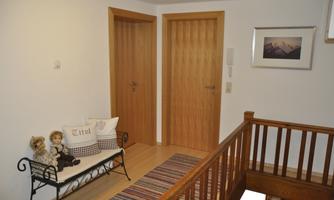 An inviting hallway with two wooden doors and a cozy bench. A picture hangs on the wall and a colorful runner lies on the floor.