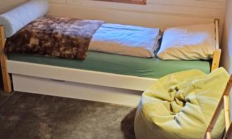 A cozy room with a bed, a bean bag, and a small table. The window lets in daylight and the walls are made of wood.