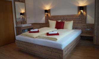 A cozy bedroom with a large bed and elegant wood paneling. The decor features red cushions and a modern light accent.