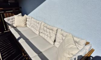 A cozy sofa with white cushions on a balcony. The walls are painted in a soft blue.