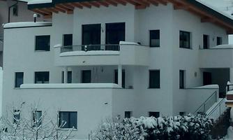 A modern, white house with a balcony, surrounded by snow. The landscape is wintery and tranquil.