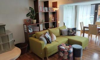 A modern living room with a green sofa and colorful cushions. There are bookshelves and a dining area with a view of the light from outside.