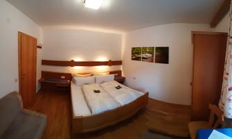 A cozy room with a double bed and bright decor. Pictures of a green landscape hang on the wall.