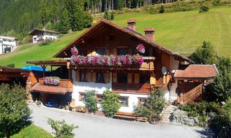 A traditional Alpine house with blooming flower boxes and a beautiful surrounding area. In the background, green forests and meadows can be seen.
