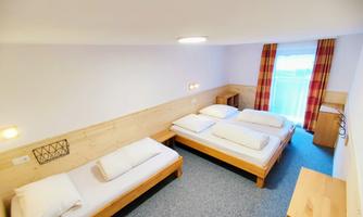 A bright room with two beds and a window with curtains. The room has a modern wood style and a cozy carpet.