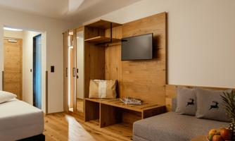 A modern hotel room with wooden elements and cozy furnishings. There is a jacket, a television, and a seating area with fruit.