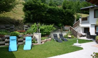 A beautiful garden with two loungers and plenty of greenery. In the background, a house and a hilly landscape can be seen.