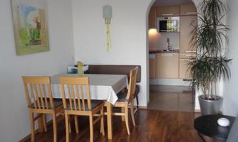 A cozy living space with a dining table and chairs. In the background, a simple kitchenette is visible.