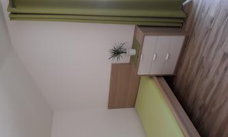 A simple bedroom with a single bed and a nightstand. The walls are white, and a green curtain complements the room.