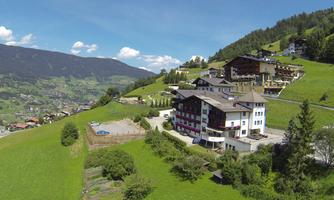 A picturesque mountain village with green hills and modern buildings. The sky is clear and bright blue.