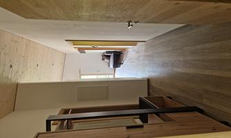 A bright hallway with wooden floors and walls. At the end of the hallway is a window and a quiet room.