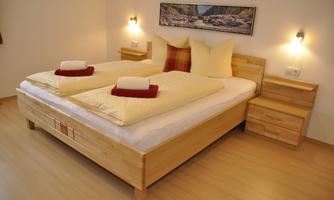 A cozy bedroom with a large double bed and stacked pillows. The warm wood decor and gentle light create an inviting atmosphere.