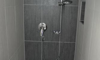 A modern shower with gray tiles and a rainforest showerhead. The space appears clean and minimalist.