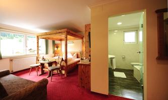 A cozy room with a double bed and a small dining area. In the background, there is a modern bathroom.
