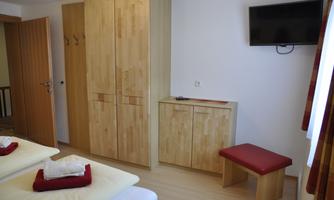 A bright room with wooden furniture, a television, and a cozy seating area. The two beds are neatly arranged with red pillows and towels.