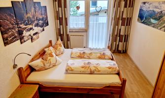 A cozy bedroom with a double bed and colorful cushions. Large windows let in plenty of light and offer a view of nature.