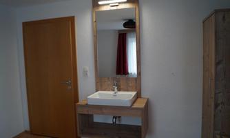 A modern bathroom with a sink and a large mirror. The walls are bright, and a wood look creates a warm atmosphere.
