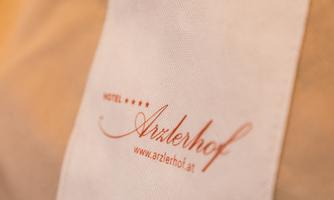A hotel towel with the logo of the hotel "Arzlerhof". The hotel's website is also printed on it.
