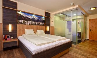 A modern hotel room with a double bed and a large window. The room features a bathroom with a glass wall and cozy wood accents.