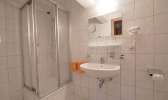 A modern bathroom with a shower, sink, and large tiles. Towels in orange decorate the room.