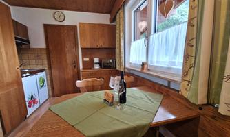 A cozy kitchen with wooden cabinets and a dining table. On the table is a bottle of wine and a green tablecloth.