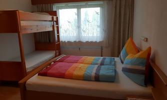 A bright room with a double bed and a bunk bed. The colorful pillows and the windows create a friendly atmosphere.