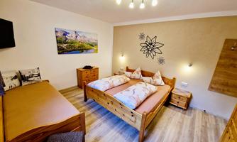 A cozy bedroom with wooden furniture, two beds, and modern lighting. A picture of a mountain landscape hangs on the wall.
