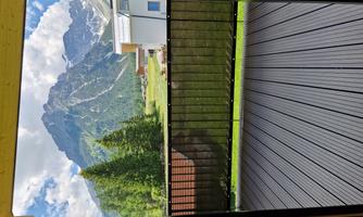 View from a balcony of majestic mountains and lush meadows. The sky is clear with a few clouds.