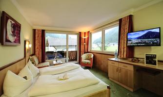 A cozy hotel room with two beds and a TV. Large windows offer a view of the surroundings.