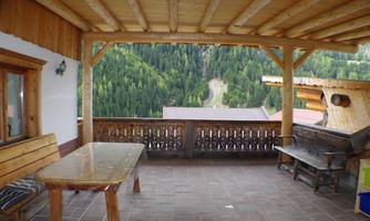 A cozy balcony with wooden furniture and a view of green mountains. The covered terrace offers an inviting spot to relax.