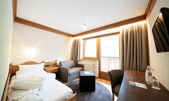 A cozy hotel room with a single bed, a sofa, and a desk. Large windows let in plenty of light and offer a view of the balcony.