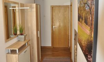 A bright hallway with a wooden floor and a colorful rug. On the wall, two mirrors and a large picture of an autumn landscape hang.