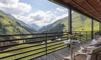 A panoramic view of green mountains and valleys from a terrace. On the table, there is a bouquet of flowers, and it is a beautiful, sunny day.