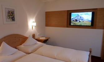 A cozy bedroom with two single beds and a modern television on the wall. The warm wood design creates an inviting atmosphere.