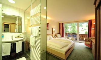 A modern hotel room with a bathroom and large windows. The room is bright and welcoming with a view of nature.