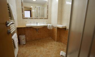 A modern bathroom with bright tiles and a large mirror. There is a shower, a sink, and a trash can visible.