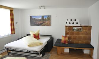 A cozy room with a pull-out bed and colorful cushions. Visible are a wooden stove and a picture on the wall.