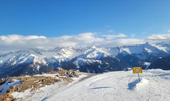 An impressive mountain landscape with snow-capped peaks and a clear blue sky. In the foreground, a ski symbol is visible.