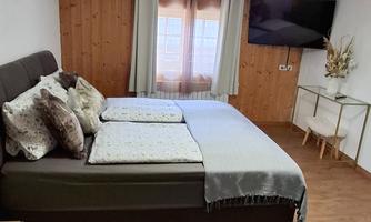 A cozy bedroom with a large bed and several pillows. There are wooden walls, a television, and a small seating area.