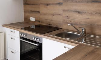A modern kitchen with white cabinets and wood elements. The cooking area consists of a stove, an oven, and a sink.