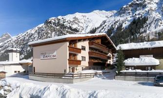 A cozy house in the winter mountains, surrounded by snow-covered peaks. Clear blue skies and serene nature create a peaceful atmosphere.