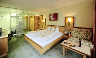 A modern hotel room with a double bed, a cozy seating area, and a bathroom area. It is brightly and invitingly furnished.
