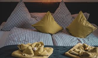 A cozy bedroom with a large bed. The pillows are checkered and in yellow, and neatly folded towels are placed on the bedspread.